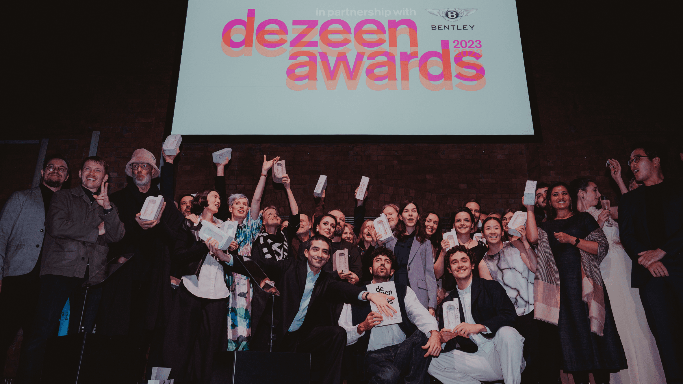 Winners of the Dezeen Awards 2024 celebrating on stage with their trophies.