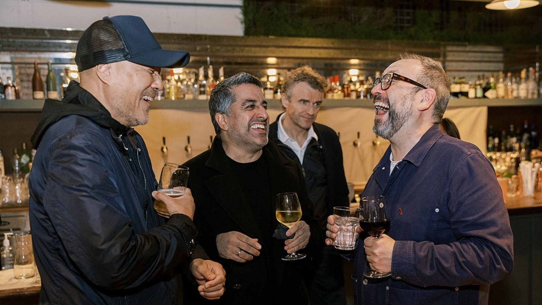 4 people at a networking event. They are holding wine glasses and are laughing.