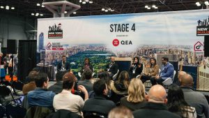 Panel discussion at New York Build Expo, featuring industry experts on Stage 4, Facilities Management Track. Audience members are engaged as panelists share insights on construction, infrastructure, and building management against the backdrop of a cityscape.