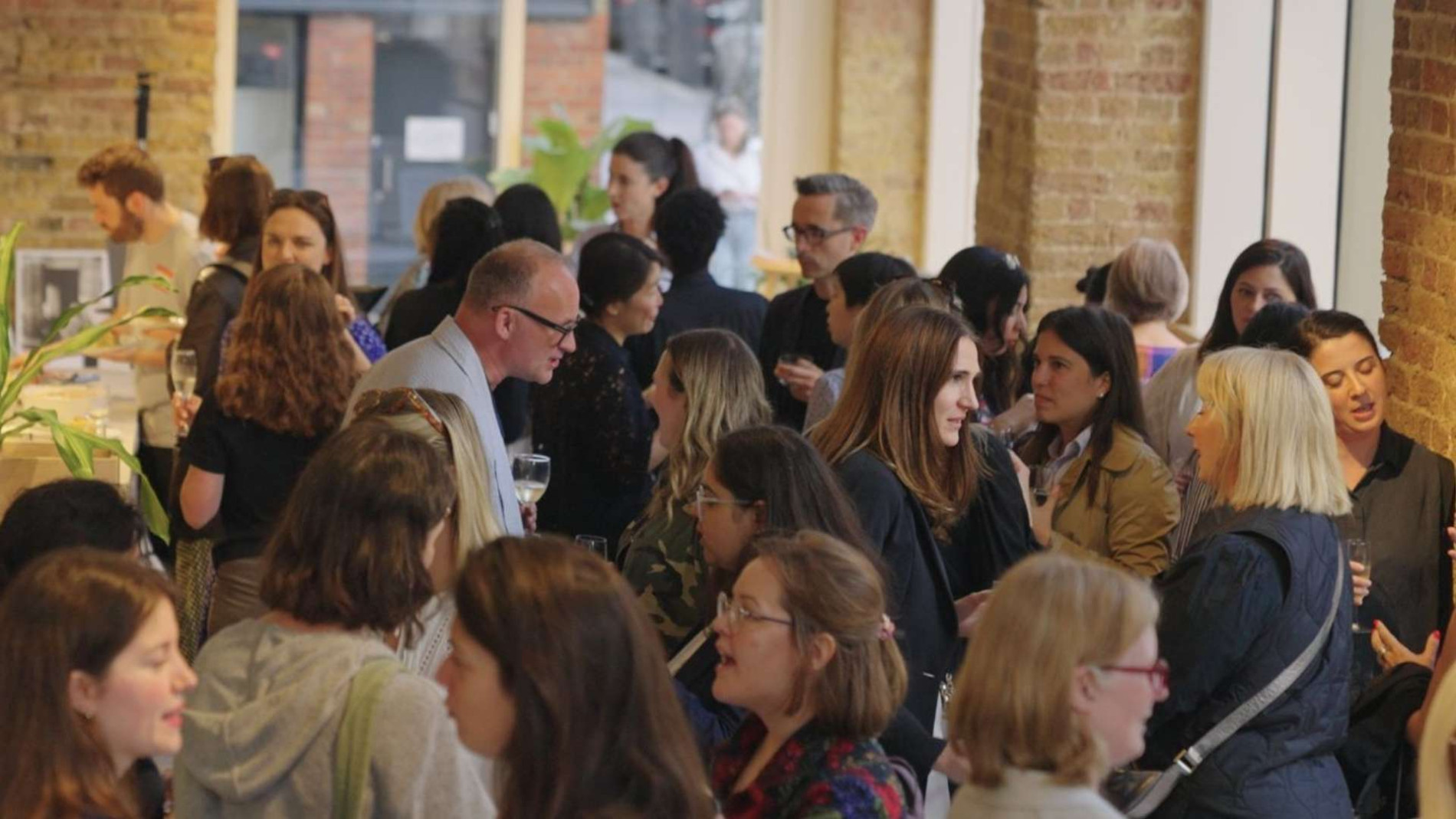 Women in Architecture networking event with attendees engaging in discussions in a modern, open space with exposed brick walls and natural light.