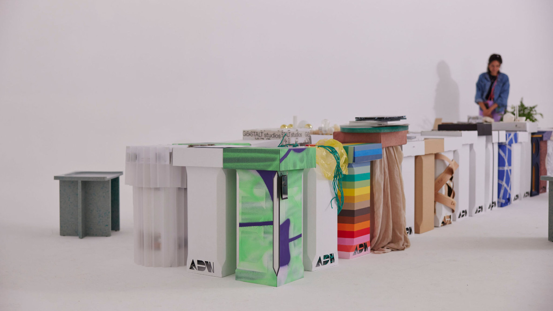 Colourful and creatively designed display stands arranged in a row with a person working in the background against a minimalist white setting.