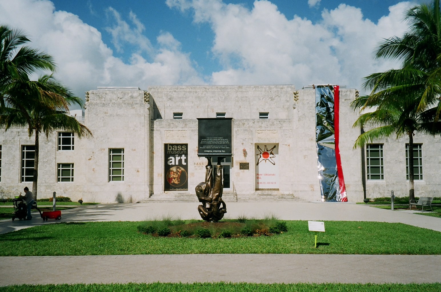 Front view of the Bass Museum of Art in Miami Beach, featuring a modern sculpture on the lawn and promotional banners on the building facade.