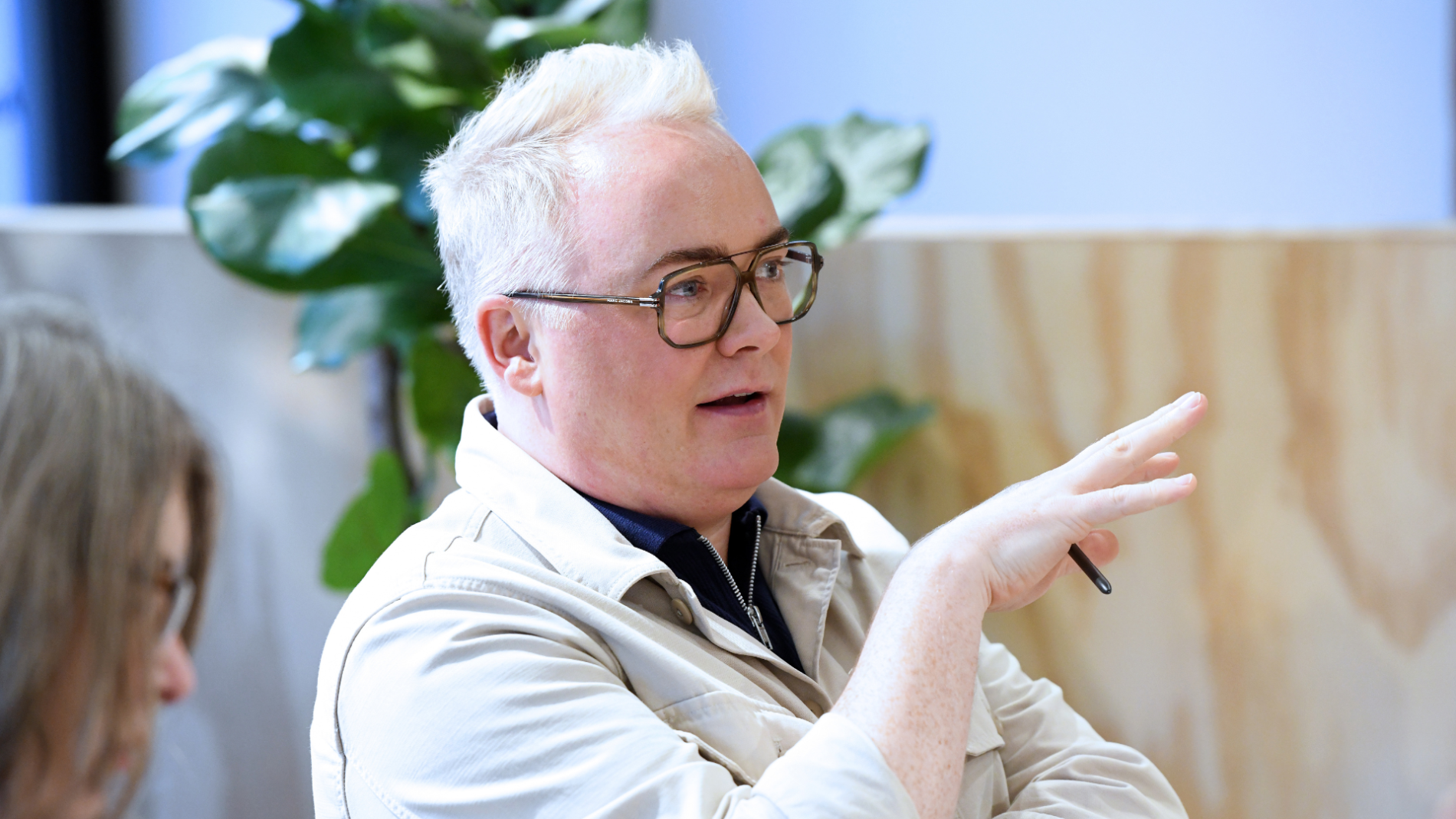 Man with blond hair and glasses gesturing while speaking in a discussion.