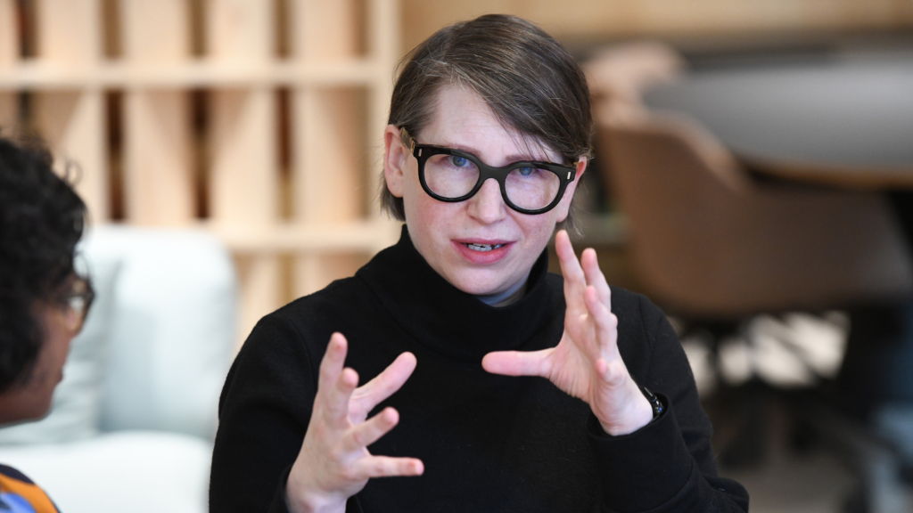 Womanin glasses and a black top gesturing while engaged in a discussion.