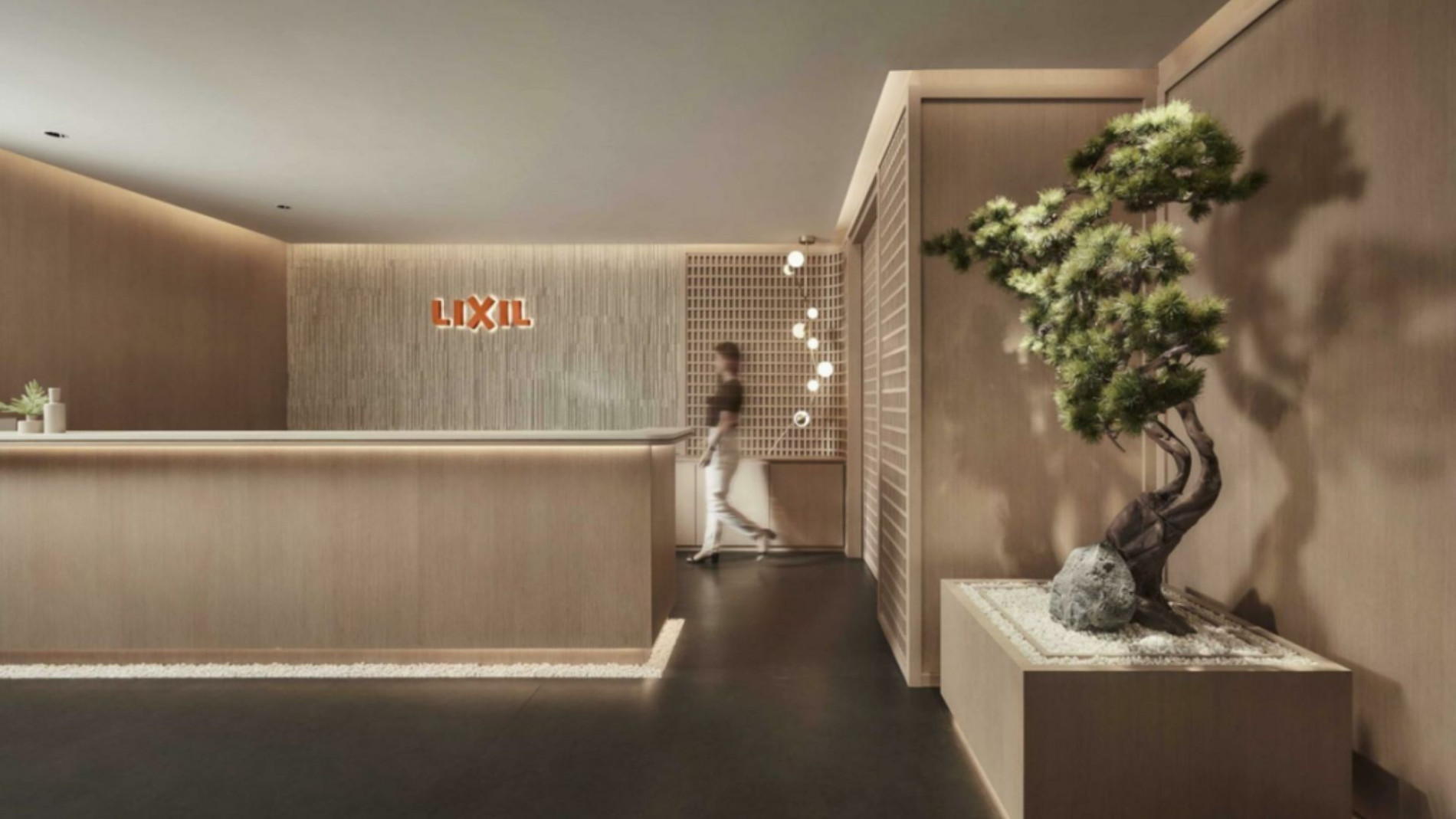 Minimalist reception area at the LIXIL Water Experience Center, featuring warm wood tones, soft ambient lighting, a bonsai tree in a zen-inspired planter, and a sleek modern desk with the LIXIL logo on the textured wall.