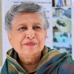 A portrait of Yasmeen Lari, a prominent architect, with short gray hair, wearing a green and gold patterned shawl.