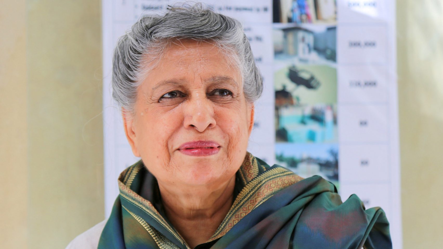 A portrait of Yasmeen Lari, a prominent architect, with short gray hair, wearing a green and gold patterned shawl.