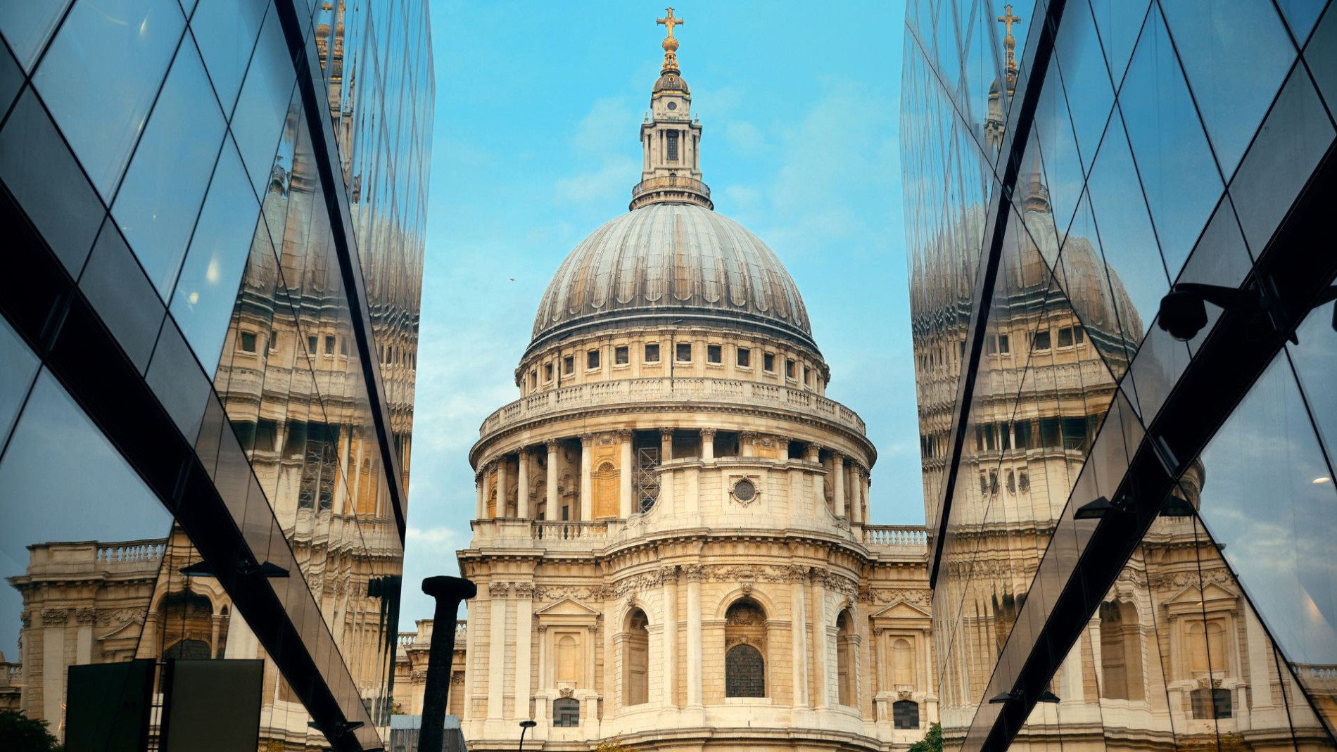 St Paul's Cathedral framed by modern glass buildings, with its reflection creating a symmetrical composition against a blue sky.