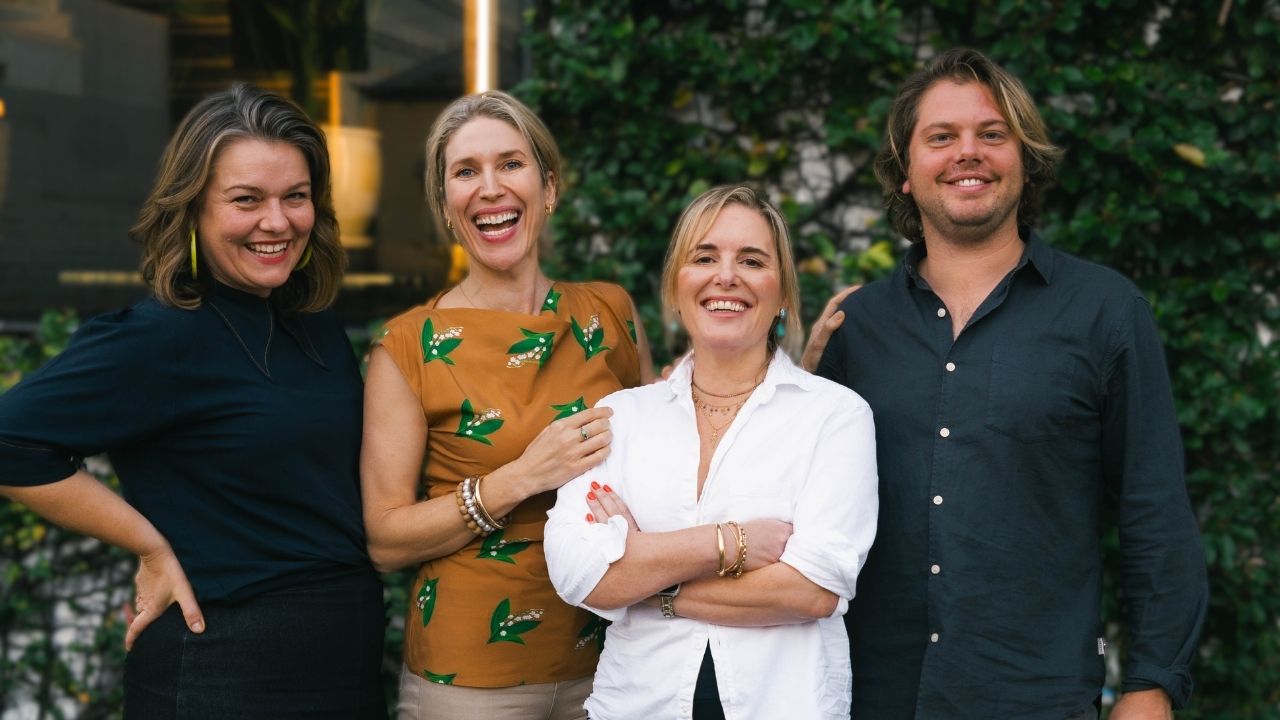 Four smiling professionals posing together outdoors in front of a green ivy-covered wall, dressed in casual business attire.