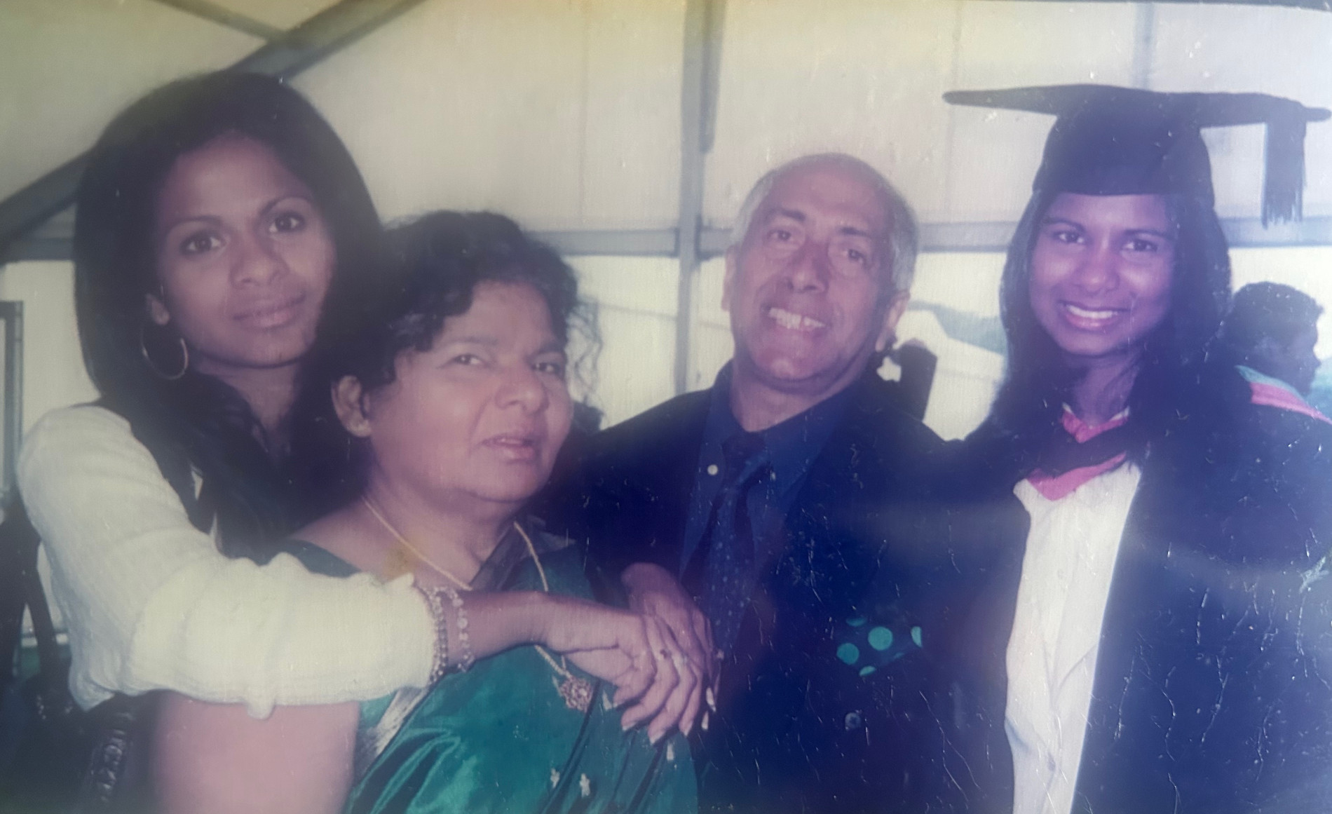 Nimi at graduation with 3 family members. She is wearing grad attire.