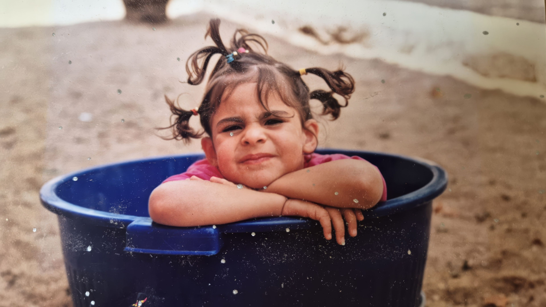 Mariana as a child. Shes in a bicket with her arms folded. Her hair is tied in 4 pigtails.