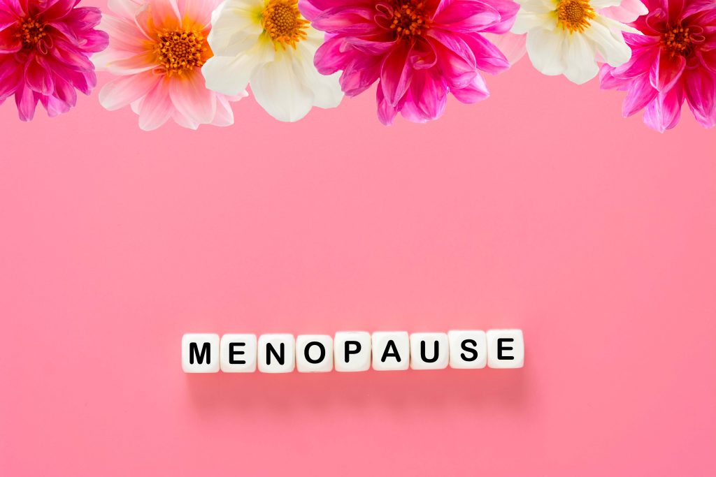 Menopause word abstract text, wooden blocks with dahlia pink flowers, over pink background, top view
