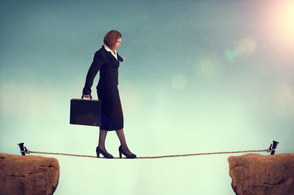 A photo of a woman in a suit holding a briefcase. She is walking across a tightrope.