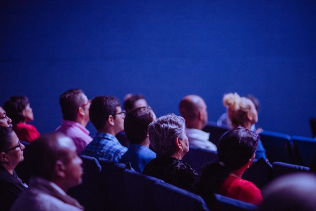 People seen from the side sitting in a theatre bathed in blue light.