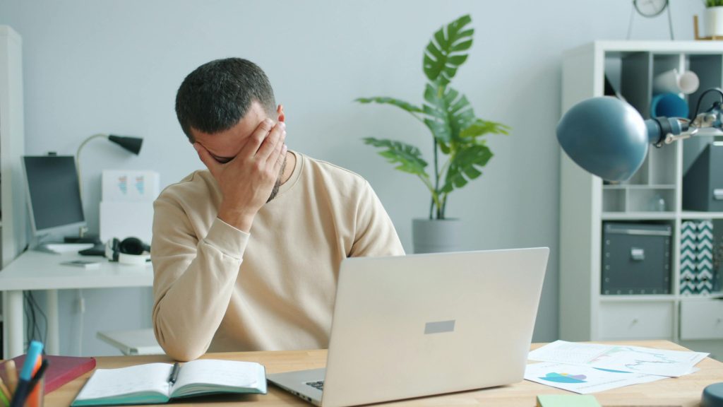 Conference producer experiencing burnout and stress while working on laptop in high-pressure production environment