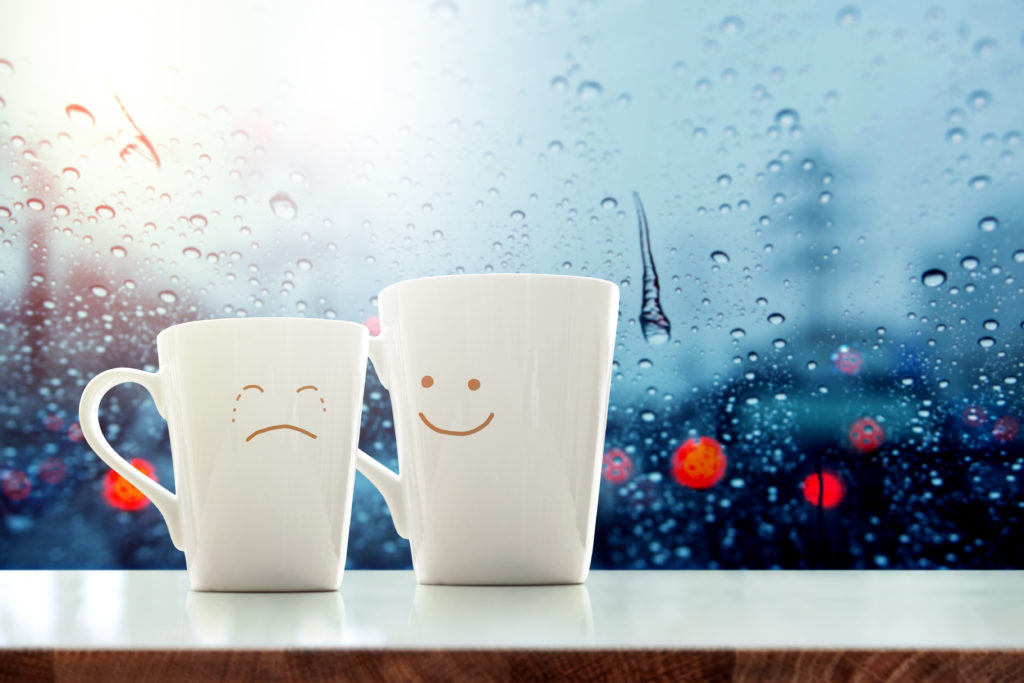 "It's ok" concept, Friend of  Coffee Mug with Sadness crying face cartoon and kindness happy face inside the room, Blurred city light and rain drop in city as outside view through glass window